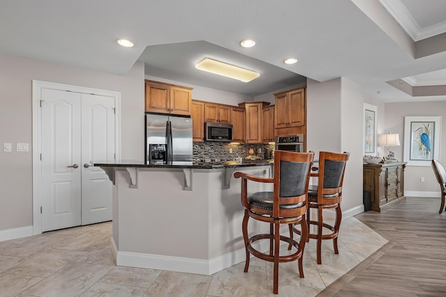 kitchen with appliances with stainless steel finishes, backsplash, ornamental molding, and a breakfast bar area