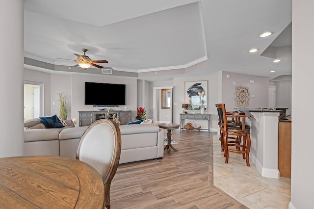 living room featuring a tray ceiling, ceiling fan, and ornamental molding