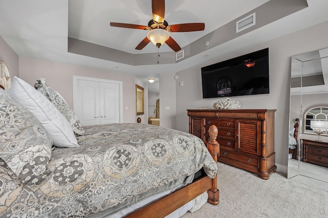 carpeted bedroom featuring a raised ceiling, ceiling fan, and a closet