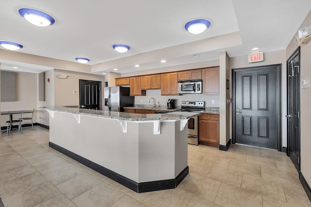 kitchen featuring a center island, sink, light stone countertops, a kitchen bar, and stainless steel appliances