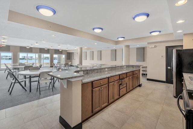 kitchen with a raised ceiling, light tile patterned floors, a large island, light stone counters, and stainless steel appliances