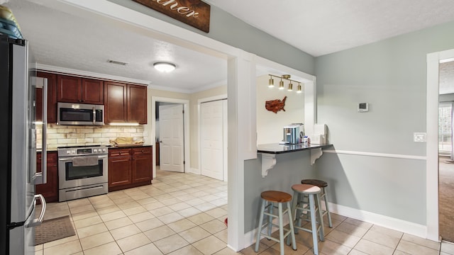 kitchen with tasteful backsplash, ornamental molding, a breakfast bar, stainless steel appliances, and light tile patterned floors