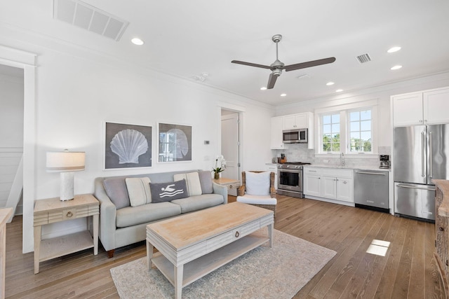 living room with crown molding, sink, ceiling fan, and light hardwood / wood-style floors