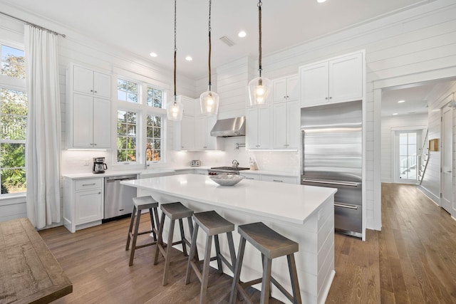 kitchen with white cabinetry, a center island, stainless steel appliances, wall chimney range hood, and a breakfast bar