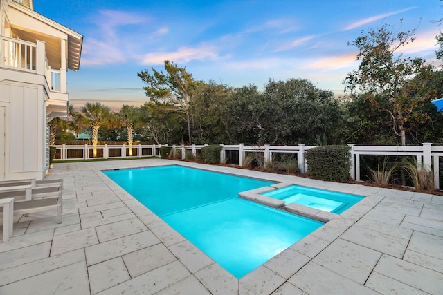 pool at dusk featuring a patio area and an in ground hot tub