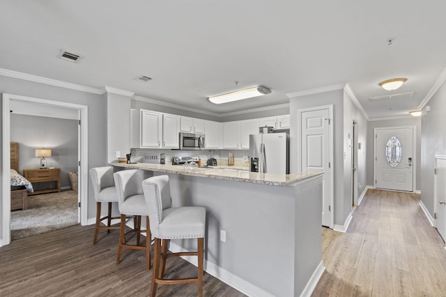 kitchen featuring kitchen peninsula, backsplash, appliances with stainless steel finishes, white cabinets, and a kitchen bar