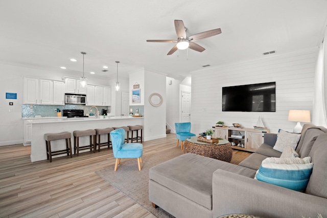 living room featuring ceiling fan, sink, light wood-type flooring, and ornamental molding