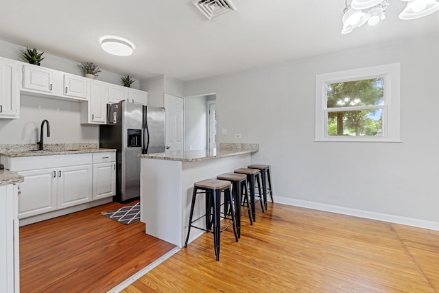 kitchen featuring sink, stainless steel refrigerator with ice dispenser, light hardwood / wood-style floors, white cabinetry, and a breakfast bar area