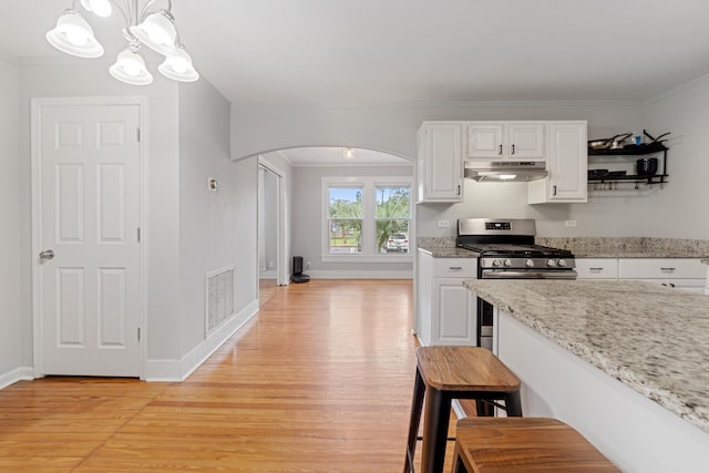 kitchen featuring white cabinetry, stainless steel gas stove, light stone countertops, decorative light fixtures, and ornamental molding