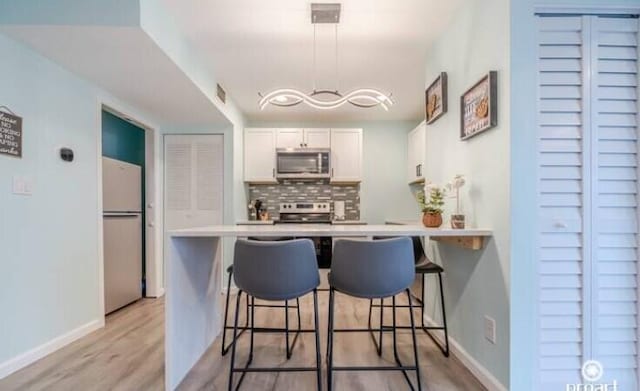 kitchen featuring a breakfast bar area, white cabinetry, appliances with stainless steel finishes, kitchen peninsula, and decorative backsplash