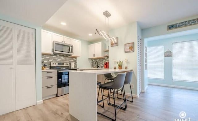 kitchen with a breakfast bar, hanging light fixtures, kitchen peninsula, stainless steel appliances, and white cabinets