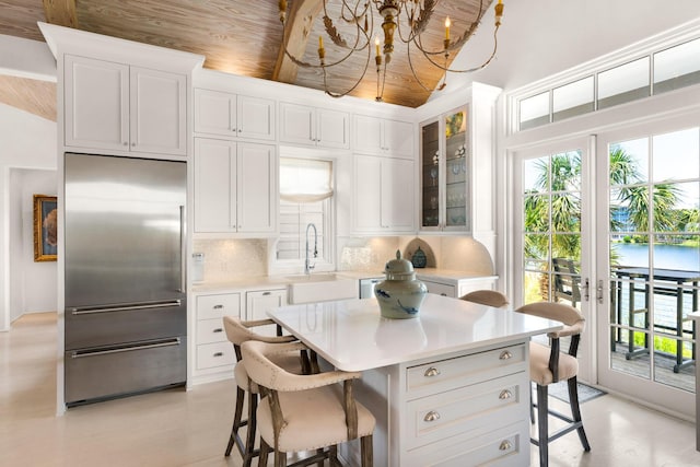 kitchen featuring tasteful backsplash, built in refrigerator, sink, and white cabinets