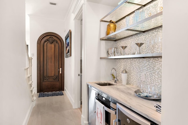 bar featuring stainless steel oven, crown molding, sink, light wood-type flooring, and tasteful backsplash