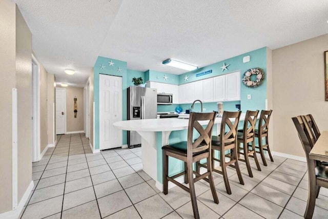 kitchen with a breakfast bar area, a textured ceiling, light tile patterned flooring, white cabinetry, and stainless steel appliances