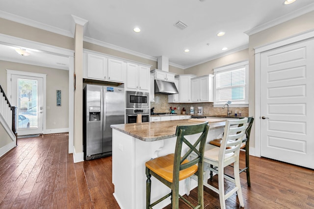 kitchen featuring a kitchen island, a kitchen breakfast bar, appliances with stainless steel finishes, white cabinets, and ornamental molding