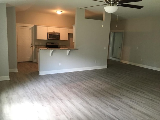 kitchen with white cabinetry, a kitchen breakfast bar, kitchen peninsula, stove, and hardwood / wood-style floors