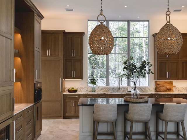 kitchen with a breakfast bar, a kitchen island, light stone countertops, and hanging light fixtures