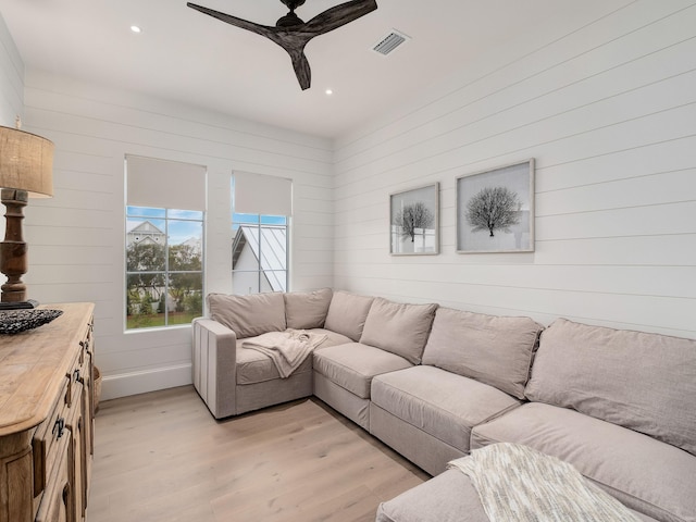 living room with light wood-type flooring, ceiling fan, and wooden walls