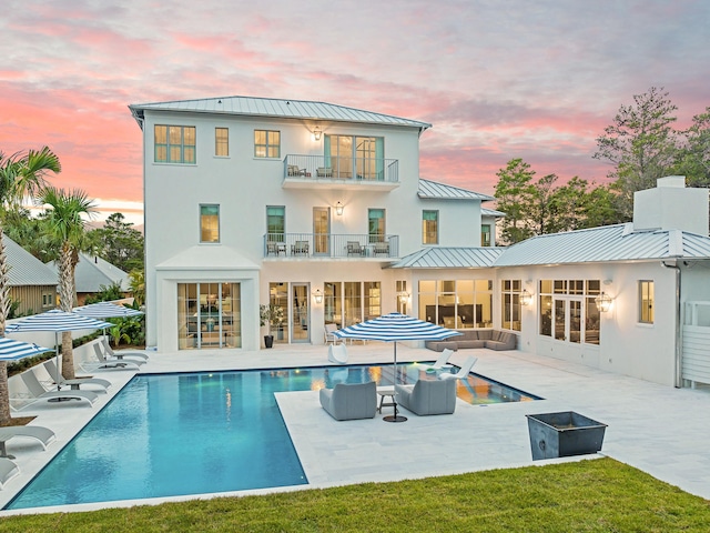 back house at dusk featuring a balcony, an outdoor hangout area, and a patio