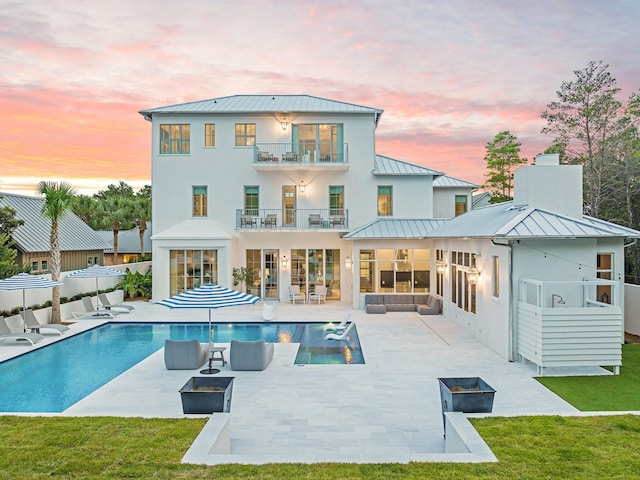 back house at dusk with a lawn, a patio area, a balcony, and an outdoor hangout area