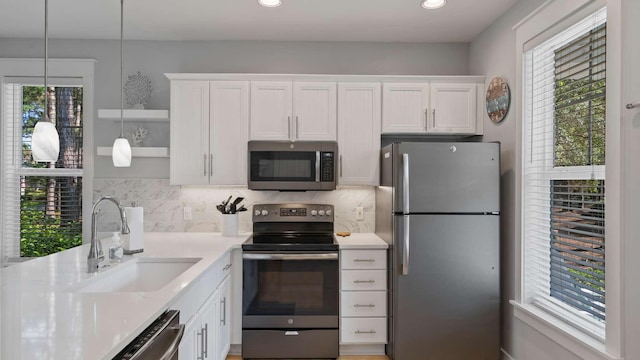 kitchen featuring pendant lighting, sink, appliances with stainless steel finishes, tasteful backsplash, and white cabinetry