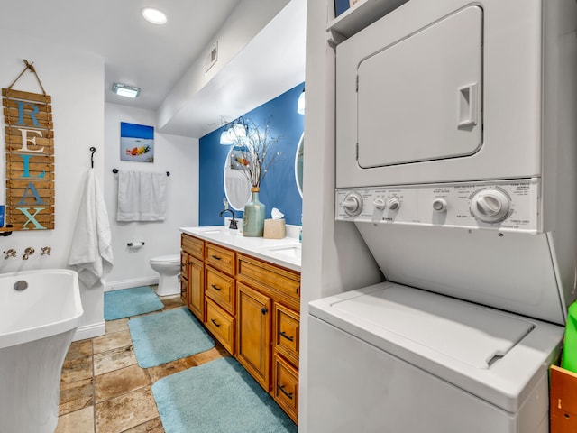 bathroom with vanity, toilet, a bathtub, and stacked washer and clothes dryer