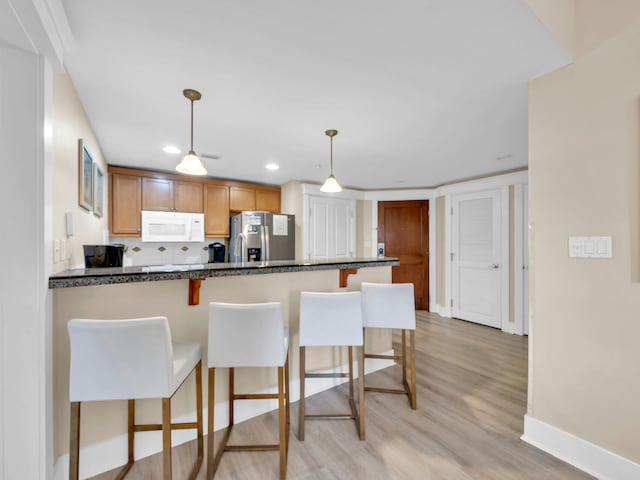 kitchen featuring dark countertops, white microwave, stainless steel fridge, a peninsula, and a kitchen bar