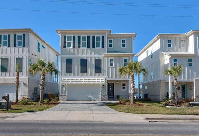 coastal inspired home with board and batten siding, an attached garage, and decorative driveway