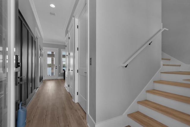 hallway featuring visible vents, light wood-style flooring, ornamental molding, baseboards, and stairs