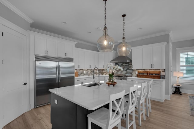 kitchen with a kitchen island with sink, a sink, ornamental molding, stainless steel built in fridge, and light wood-style floors