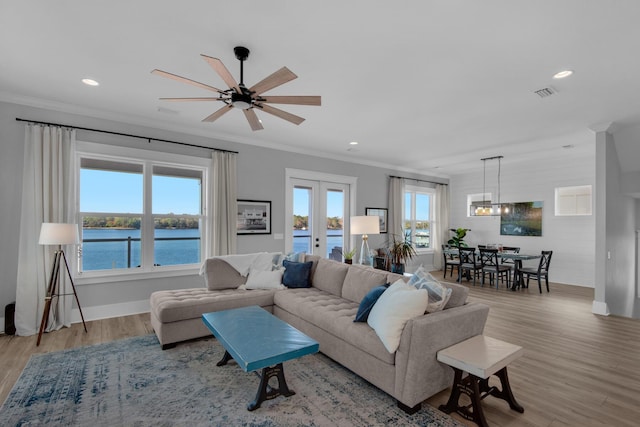 living area with crown molding, light wood-style floors, visible vents, and a water view