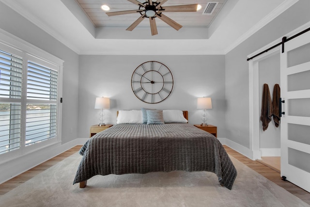 bedroom featuring a barn door, wood finished floors, visible vents, and a raised ceiling