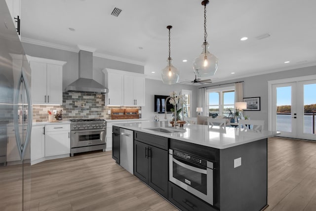 kitchen featuring a sink, wall chimney range hood, french doors, appliances with stainless steel finishes, and light countertops