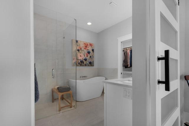 full bath featuring vanity, visible vents, a soaking tub, a stall shower, and tile walls