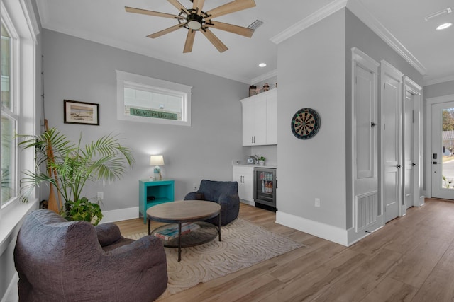 sitting room with crown molding, baseboards, wine cooler, light wood-type flooring, and a bar