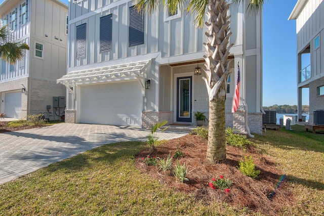 view of front facade featuring decorative driveway, a garage, brick siding, and central AC