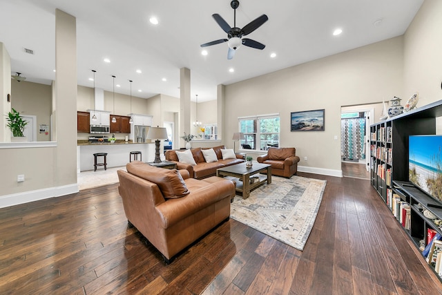 living room featuring ceiling fan with notable chandelier, dark hardwood / wood-style flooring, and a towering ceiling