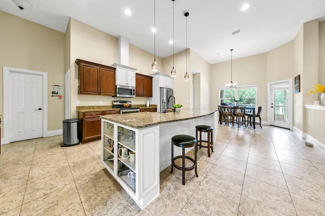 kitchen with appliances with stainless steel finishes, light stone counters, pendant lighting, a center island with sink, and a breakfast bar area