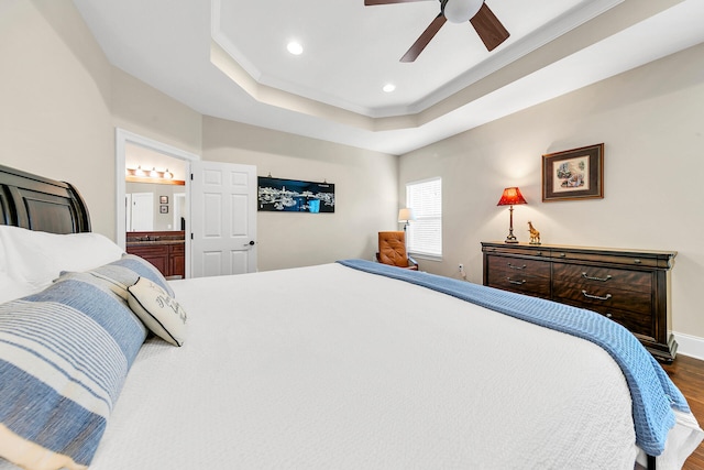 bedroom featuring connected bathroom, ceiling fan, dark wood-type flooring, a tray ceiling, and ornamental molding