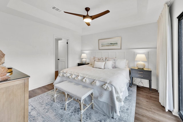 bedroom with ceiling fan, a tray ceiling, and hardwood / wood-style floors