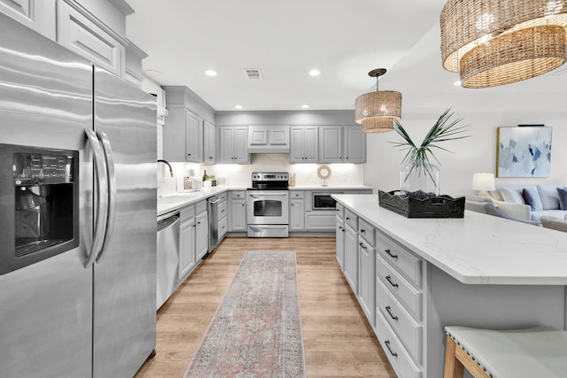 kitchen featuring light stone counters, light hardwood / wood-style floors, hanging light fixtures, gray cabinets, and appliances with stainless steel finishes