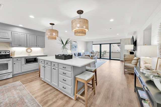 kitchen with appliances with stainless steel finishes, light hardwood / wood-style flooring, decorative light fixtures, and a kitchen island