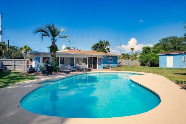 view of pool featuring a lawn, a patio, and a storage unit