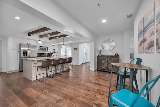 kitchen with light stone countertops, stainless steel appliances, pendant lighting, beamed ceiling, and white cabinetry