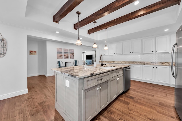 kitchen with a kitchen island with sink, sink, decorative light fixtures, light stone counters, and white cabinetry