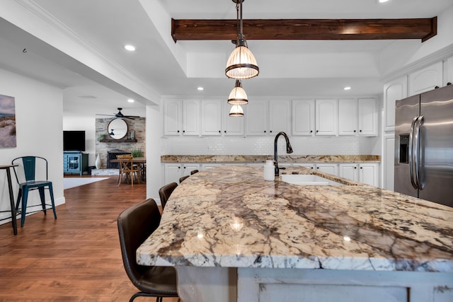 kitchen with white cabinetry, a stone fireplace, stainless steel refrigerator with ice dispenser, decorative light fixtures, and decorative backsplash