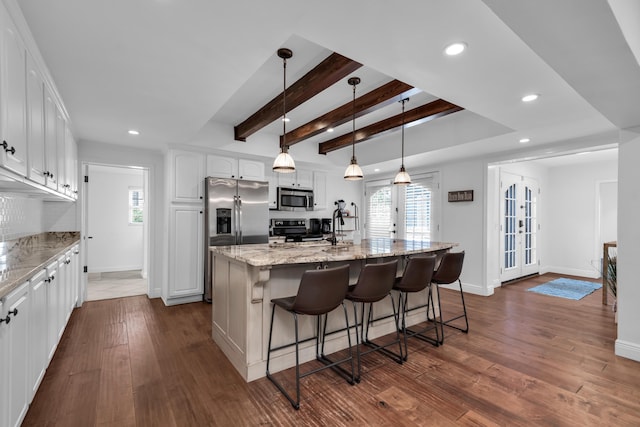 kitchen featuring appliances with stainless steel finishes, french doors, light stone counters, a center island with sink, and white cabinets