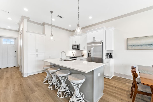 kitchen featuring a center island with sink, white cabinets, sink, hanging light fixtures, and appliances with stainless steel finishes