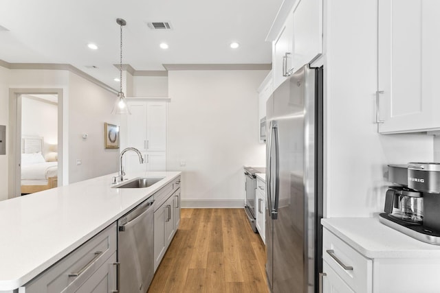 kitchen with white cabinets, sink, light wood-type flooring, appliances with stainless steel finishes, and decorative light fixtures