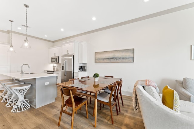 dining space featuring crown molding, sink, and light hardwood / wood-style flooring